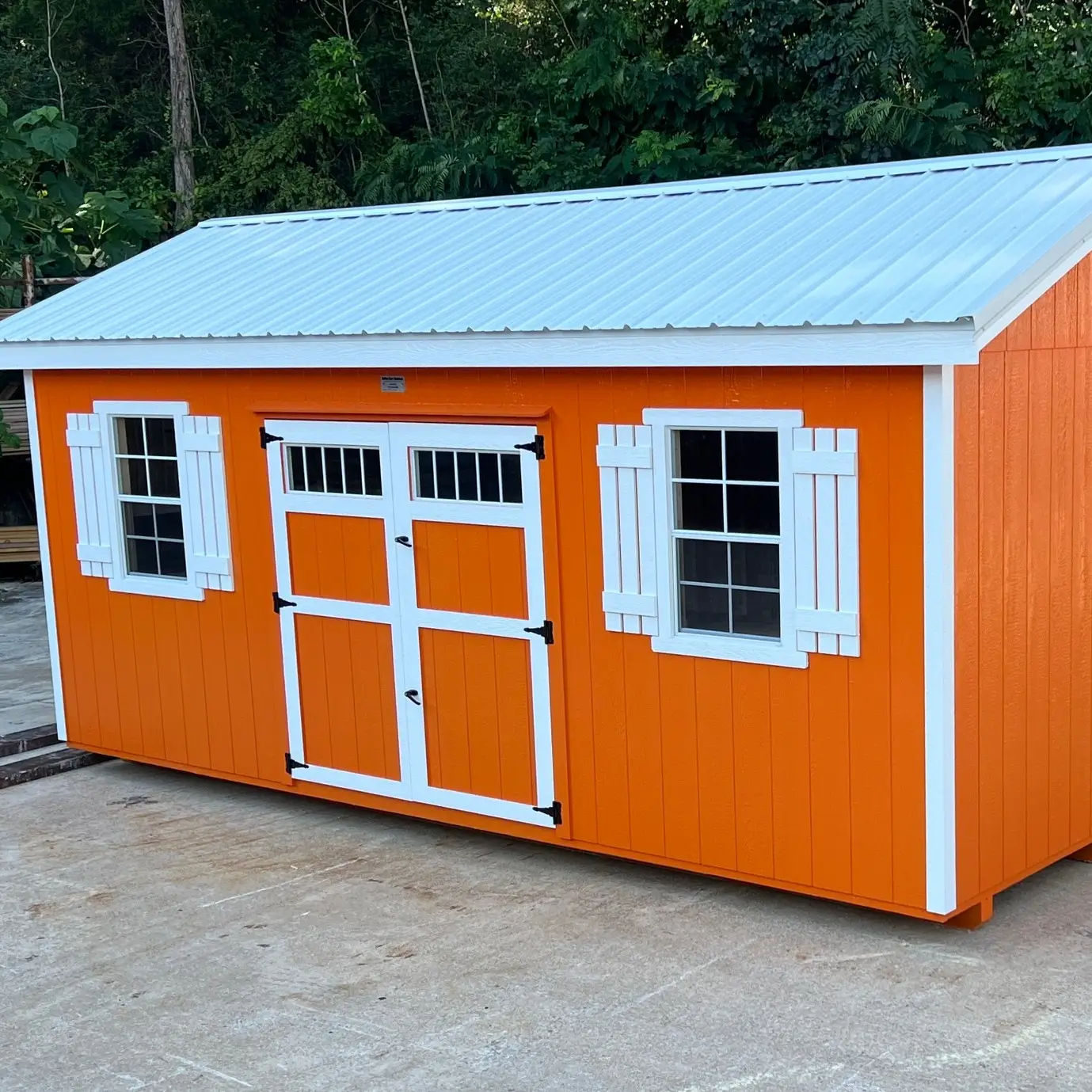 Bright orange custom storage shed with white trim, metal roof, double barn doors, and two windows.